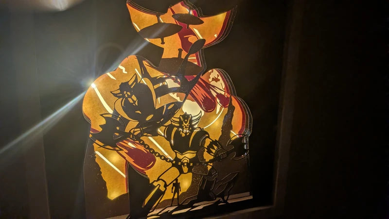 Cadre lumineux en papier découpé représentant le robot Goldorak, style rétro-gaming.