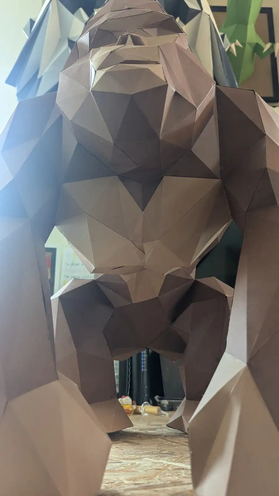 Sculpture papercraft gorille XL en papier marron posée sur une table d’atelier, vue de profil avec ses formes anguleuses