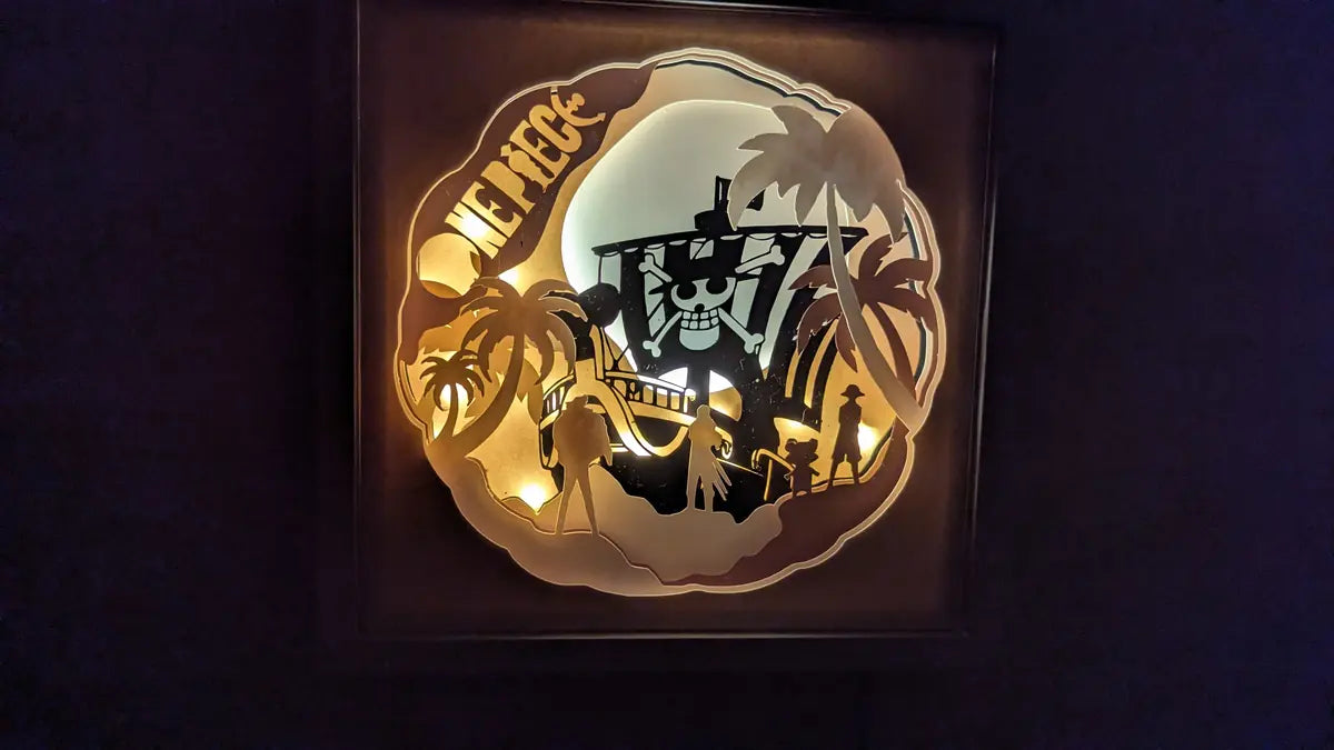 Lightbox One Piece découpée en couches de papier avec le Thousand Sunny et les personnages Luffy, Zoro et Chopper – scène lumineuse artisanale