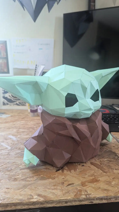 Figurine en papercraft low poly de Grogu (Baby Yoda) vue de trois quarts, mettant en valeur ses grandes oreilles et sa robe marron.