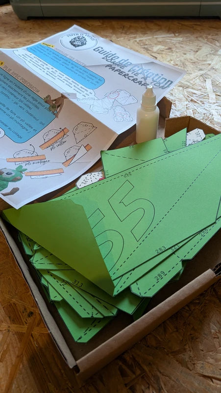 Présentation de la boite d'un kit ouvert, comprenant la notice explicative, 20ml de colle blanche cleocol à prise rapide et les pièce numérotées et pré-découpées pour l'assemblage du modèle par Paper In Events