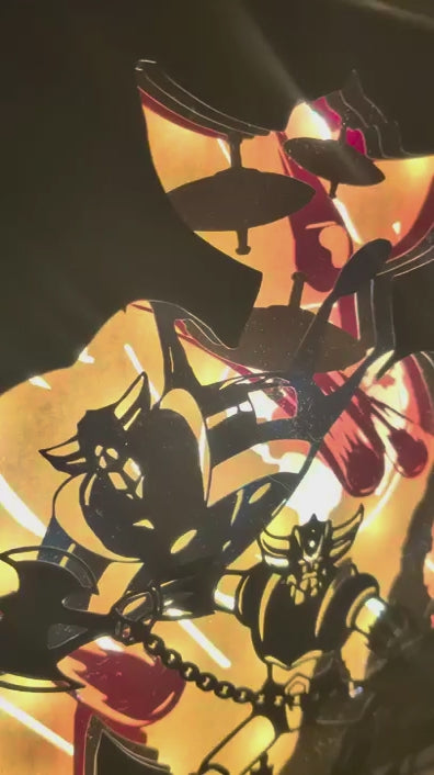 Travelling vidéo détaillé sur les couches de papier découpé superposées d'une lampe Goldorak faite main, mettant en valeur les détails du robot et de l'arrière-plan lumineux.