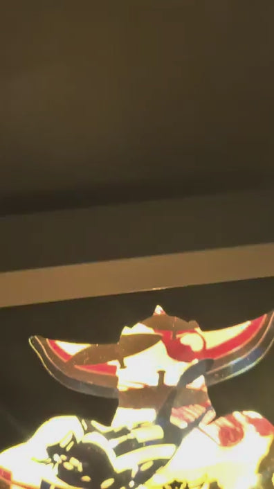 Vidéo gros plan d'une lightbox artisanale Goldorak en papier découpé éclairée de l'intérieur, montrant le robot en action avec ses armes, sur un fond spatial jaune et rouge.